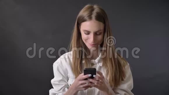 年轻酷女孩正在智能手机上绑信息微笑交流理念灰色背景视频的预览图