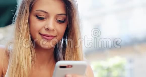 年轻女子坐在咖啡馆里使用智能手机触摸屏夏日时光拍摄红色史诗视频的预览图