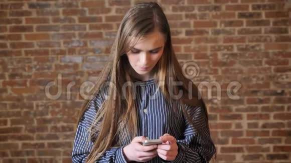 年轻漂亮的女孩正在看她的智能手机交流概念放松概念砖背景视频的预览图