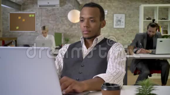 年轻的非洲女商人正在办公室里用手提电脑打字喝着咖啡同事们正在与科技建立联系视频的预览图