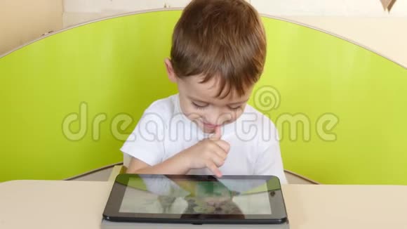 男孩坐在桌子上看着电子平板电脑摸着手微笑着视频的预览图
