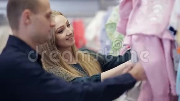 年轻快乐的孕妇在婴儿商店里挑选新生的衣服视频的预览图