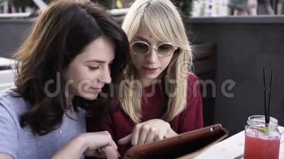 两个女朋友在户外咖啡馆里用平板电脑放大视频的预览图