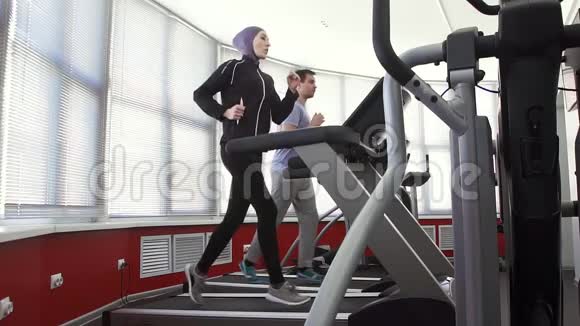 女运动员戴头巾在跑步模拟器和一个男人在健身房视频的预览图