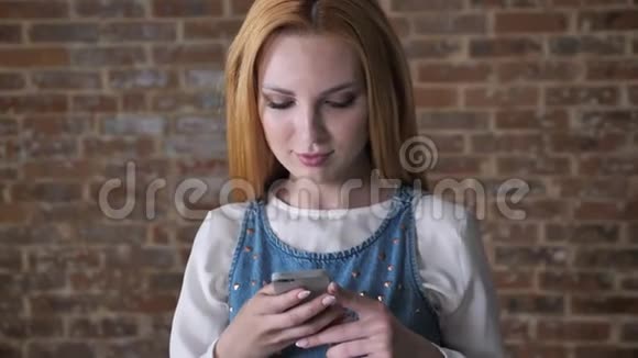 年轻迷人的金发女孩正在智能手机上输入信息砖背景理念视频的预览图