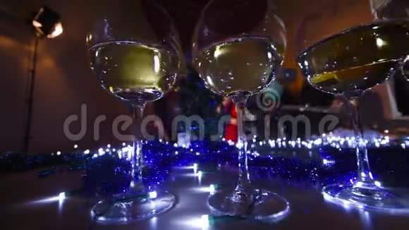 在圣诞灯光背景下的桌子上放着香槟或葡萄酒的漂亮眼镜视频的预览图