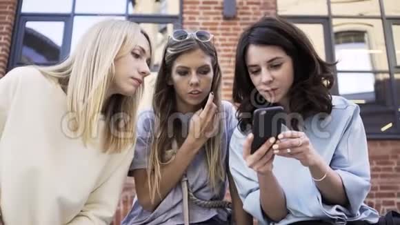 三个女人看着一个智能手机屏幕坐在夏街放大视频的预览图