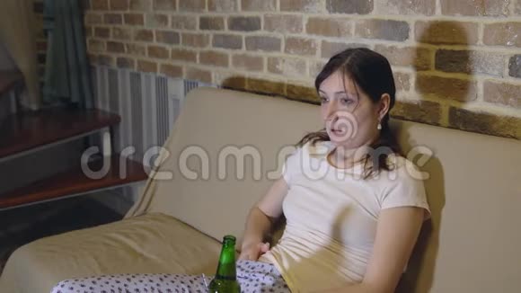 在电视前沙发上喝啤酒的年轻女子视频的预览图