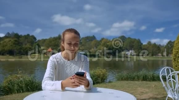 金发女孩在河边咖啡馆的餐桌上发短信视频的预览图