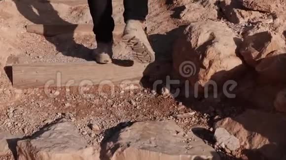 男性腿在沙漠楼梯上爬上去慢动作人类踏上沙漠岩石山后景站起来职业道路视频的预览图