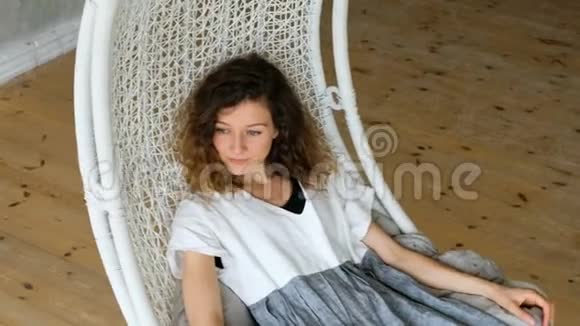 穿亚麻布连衣裙的年轻欧洲女孩在阁楼公寓的吊床上摇摆美丽的女人躺在吊床上视频的预览图