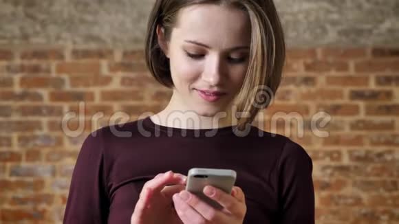年轻漂亮的女孩正在智能手机上输入信息看着摄像机微笑着交流观念砖头视频的预览图