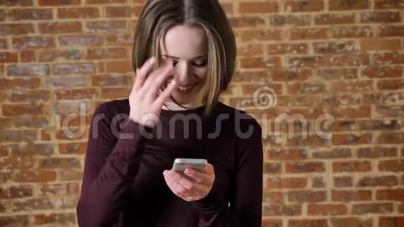 年轻开朗的女孩在她的智能手机上输入信息微笑交流理念砖背景视频的预览图