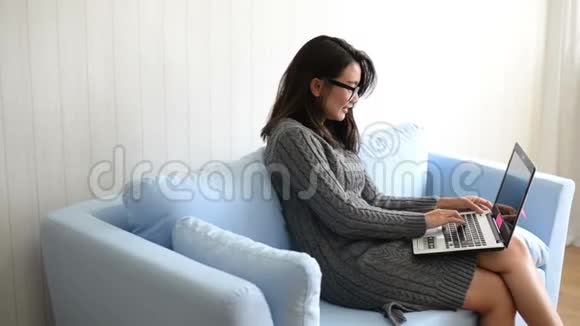 快乐的年轻女子坐在沙发上在家里用笔记本电脑视频的预览图