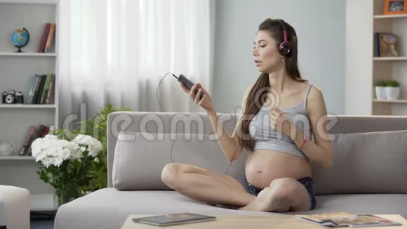 孕妇坐在沙发上用手机听轻松的音乐视频的预览图