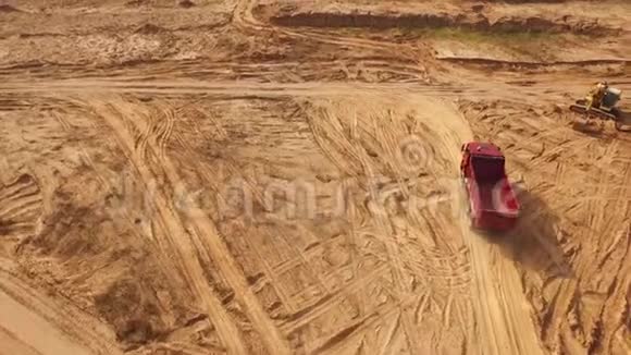 在沙漠或沙丘中黄色挖掘机附近的沙地上移动的空大红色卡车的视图美丽的景色视频的预览图