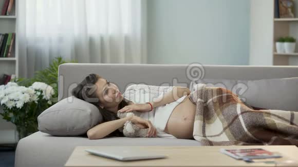 怀着泰迪熊躺在沙发上的女人对她未来孩子的想法视频的预览图