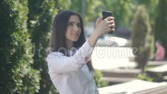 年轻女子白天在户外用智能手机拍照那个女孩在下午做了一个自我介绍视频的预览图
