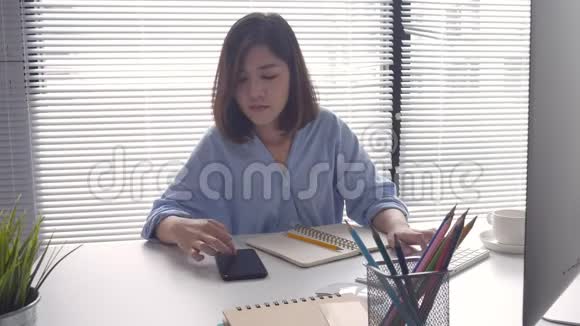 漂亮的聪明商务亚洲女人穿着智能休闲服在笔记本电脑或电脑上工作使用智能手机视频的预览图