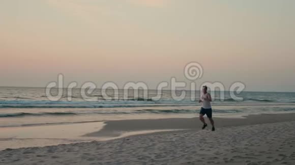 运动员在海滩上慢跑日落时在慢车上沿着海岸跑步视频的预览图