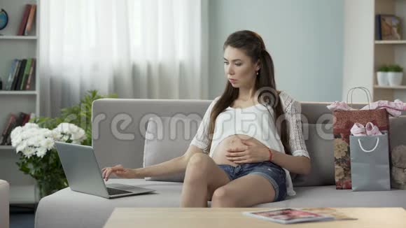 怀孕的女性看着笔记本电脑屏幕在网上买东西购物视频的预览图