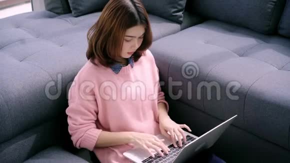 年轻的亚洲女人为她的生意做研究工作微笑的女人坐在沙发上放松一边浏览网上购物视频的预览图