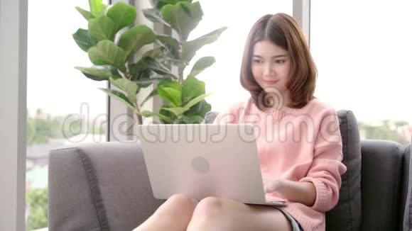 漂亮的亚洲女人在客厅里躺在沙发上用电脑或笔记本电脑视频的预览图