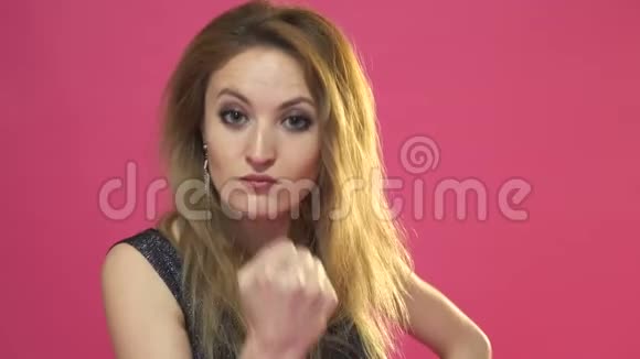 这位年轻漂亮的女士用拳头威胁的肖像被孤立在粉红色上视频的预览图