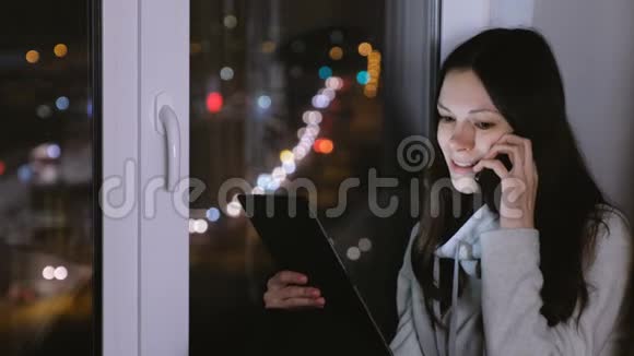 女人在手机上说话笑着看着平板电脑坐在窗台上视频的预览图