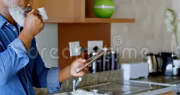 在厨房里喝黑咖啡的时候使用数码平板电脑的老人视频的预览图