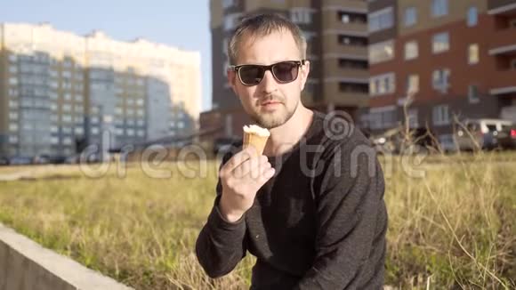 一个戴太阳镜的男人在高层建筑的背景下吃冰淇淋戴太阳镜的男人的肖像视频的预览图