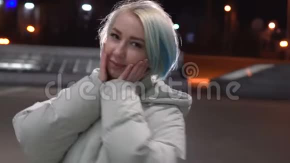 一位年轻的金发女郎穿着一件白色的时尚夹克晚上走在废弃的中央大街上视频的预览图