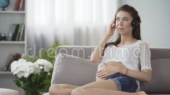 年轻的女伴戴着耳机听音乐轻轻地摸着肚子视频的预览图