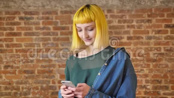 黄发型的年轻美女打电话对着镜头微笑站在砖背景附近开心视频的预览图