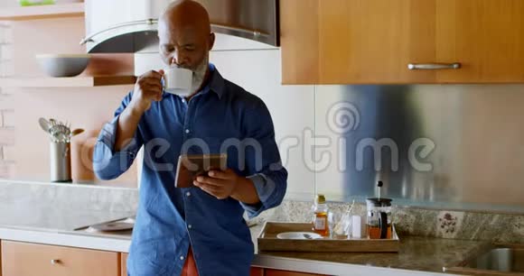 在厨房里喝黑咖啡的时候使用数码平板电脑的老人视频的预览图