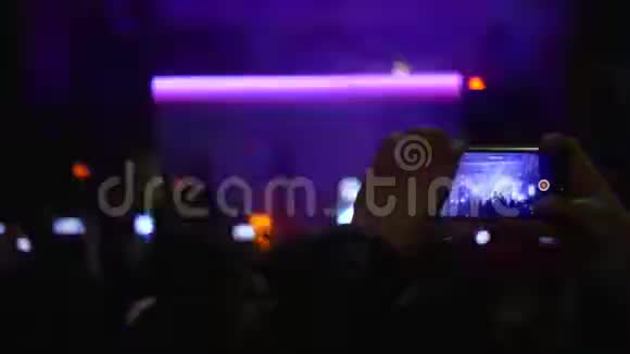 手里拿着智能手机的歌迷们在生动的舞台灯光下欣赏现场音乐视频的预览图