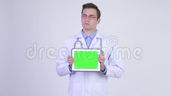 年轻快乐的帅哥医生一边看着数码平板电脑一边思考视频的预览图