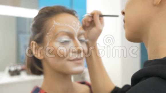 一位专业的化妆师在模特的脸上画身体艺术为选美比赛做准备相机在移动视频的预览图