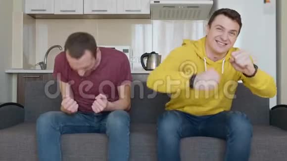 两个人坐在沙发上看电视上的足球比赛享受他们最喜欢的球队的胜利视频的预览图