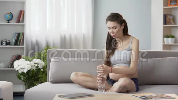 期待妇女坐在沙发上喝水保持水平衡医疗保健视频的预览图