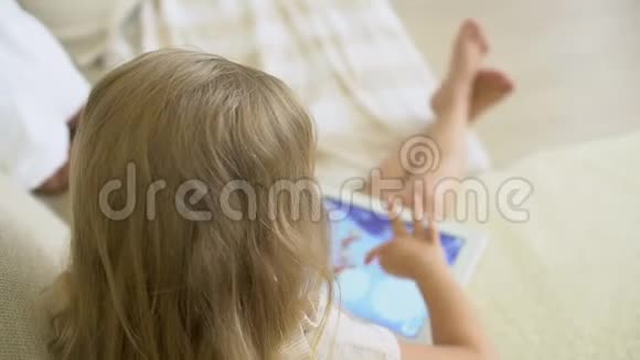 孩子在家里用平板电脑看ang儿童使用现代笔记本电脑平板电脑在沙发上小女孩在玩视频的预览图