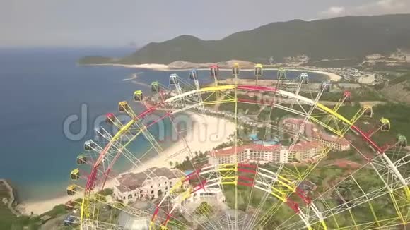 无人机在海洋和山体景观的游乐园中观看五颜六色的摩天轮大型摩天轮游乐园视频的预览图