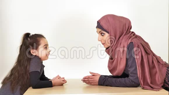年轻漂亮的母亲和她的小女儿戴着头巾看着对方镜头笑着说家庭幸福视频的预览图