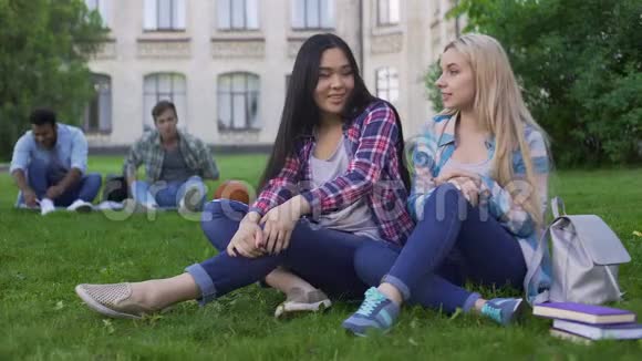 年轻漂亮的女人坐在大学附近的草坪上微笑着看着男人视频的预览图