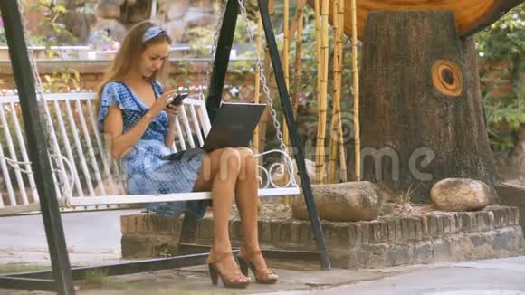 女孩坐在公园的智能手机上摇摆短信视频的预览图