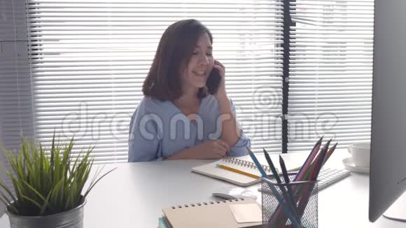 漂亮的聪明商务亚洲女人穿着智能休闲服在笔记本电脑或电脑上工作使用智能手机视频的预览图