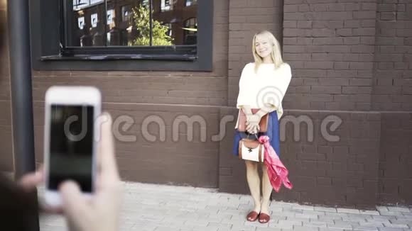女摄影师用手机拍一个金发模特的照片视频的预览图