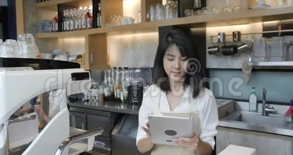 年轻的亚洲咖啡师在咖啡店休息时使用平板电脑视频的预览图