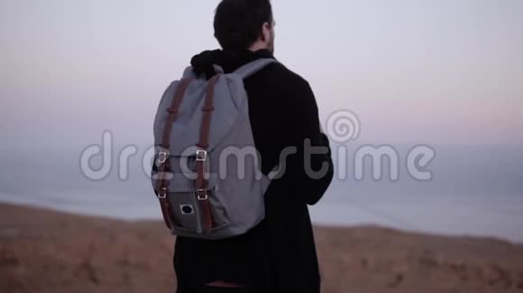 一个背着背包的人独自站在黄昏的沙漠里慢动作旅行者看着夕阳的天空寻找灵感视频的预览图