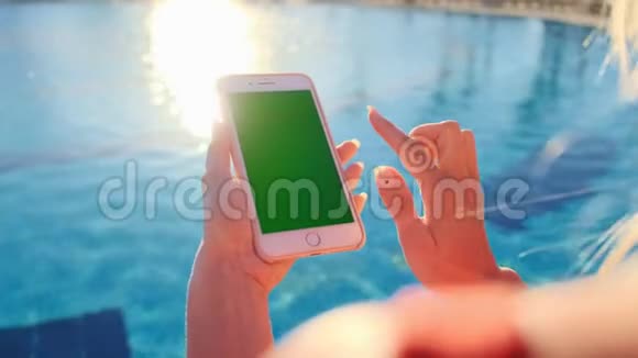 在游泳池附近放松时用手机关闭女孩的绿色屏幕手握智能手机镀铬视频的预览图